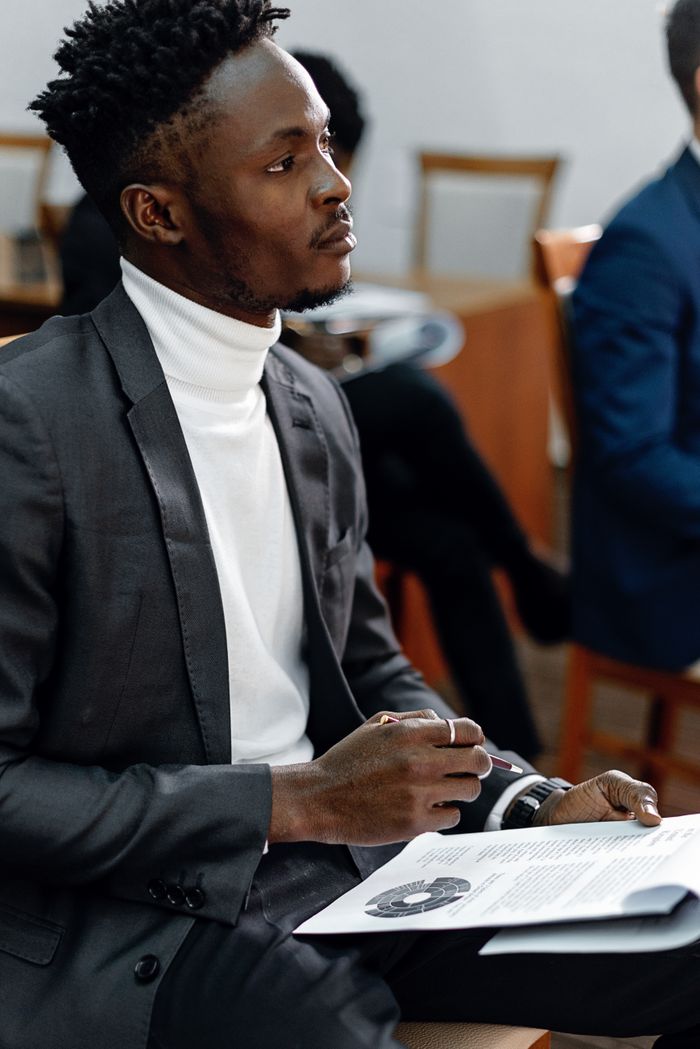 Young professional in black suit attentively listening during a presentation, holding documents.